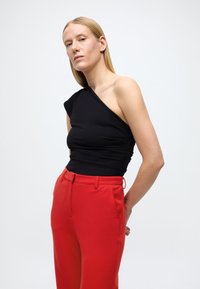 Schwarzes One-Shoulder-Oberteil aus glattem Stoff, kombiniert mit hoch taillierter roter Hose mit Seitentaschen und schlanker Passform.