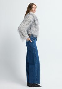 Grauer strukturierter, cropped Pullover mit fransigen Kanten, kombiniert mit hochtaillierten blauen Denim-weitbeinigen Jeans und schwarzen Ankle Boots.