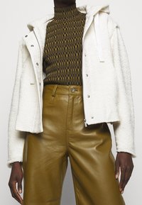 Biała pikowana kurtka z kapturem, na zamek błyskawiczny i srebrnymi napami, na brązowej i czarnej wzorzystej bluzce. Oliwkowe skórzane spodnie z wysokim stanem.