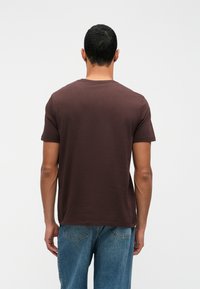 Hnedé tričko s krátkym rukávom a okrúhlym výstrihom, vyrobené z mäkkého materiálu. Navrhnuté s voľným strihom a rovnou spodnou hranou.