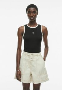 Zwarte mouwloze tanktop met witte afwerking en klein logo, gecombineerd met licht khakikleurige shorts met voorzakken en zichtbare stikdetails.