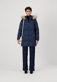 Tumsas jūras spēku pūkains mētelis ar kažokādas oderi kapucē, ar rāvējslēdzēju, elastīgām aprocēm un divām priekšējām kabatām. Saskaņots ar tumšiem platūdens biksēm un melnām zābakiem.