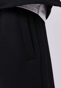 Zwarte broek heeft een gladde stoftextuur, zijzakken, een vlakke voorkant en subtiele naaddetails, wat zorgt voor een schone en moderne uitstraling.