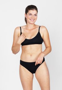 Zwarte bikini set met een driehoekig topje met dunne bandjes en laag uitgesneden broekjes. Gemaakt van gladde, rekbare stof. Eenvoudig ontwerp.