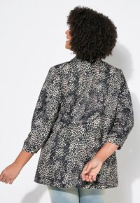 Camisa de estampado de leopardo con mangas de tres cuartos, tela ligera y un corte holgado. La paleta de colores incluye tonos negros y beiges.
