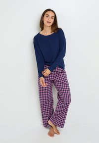 Chemise à manches longues navy assortie à un pantalon large à carreaux rose et navy, présentant une coupe décontractée et une texture de tissu douce.