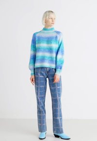Multicolored knit sweater in blue and green ombre, paired with light blue denim jeans featuring silver studs and a checkered pattern.