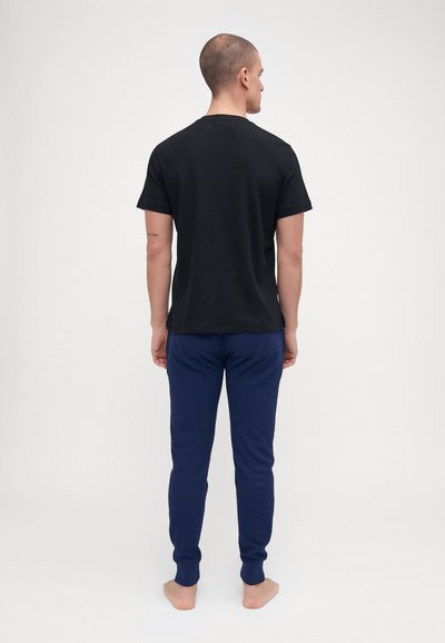 T-shirt preto de manga curta combinado com calças de jogging azul marinho. O tecido parece suave; as calças têm punhos ajustados. Exibido de costas.