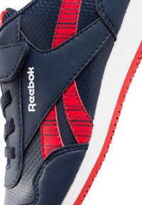 Zapatilla deportiva Reebok con un upper sintético azul marino y rayas rojas, cierre de cordones y una suela blanca con acentos rojos.
