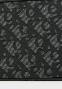 Tessuto nero con un motivo testurizzato di lettere intrecciate, arricchito da un design grigio a contrasto che aggiunge profondità e dimensione.