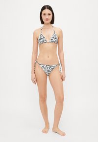 Svart og hvit blomsterbikini med trekantet topp og justerbare slipsider, som har en klassisk design og en glatt tekstur.