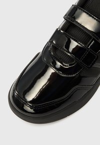 Μαύρο παπούτσι από δέρμα λάκας με ομαλή υφή, διαθέτει τρεις ρυθμιζόμενους ιμάντες Velcro και στιβαρή μαύρη ελαστική σόλα.