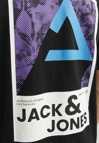 T-shirt nera con una grande grafica triangolare blu su uno sfondo a motivi viola. Il testo recita "Capi Essenziali Esteticamente Disegnati."