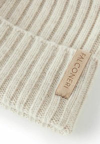 Beige ribbet strikhue med en blød tekstur, prydet med et lædermærke mærket "FALCONERI." Designet er simpelt og klassisk i stil.