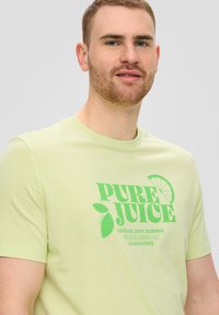 Lichtgroene T-shirt van katoen met een bedrukt ontwerp met "PURE JUICE" en citroengrafieken in donkerder groen. Korte mouwen, standaard pasvorm.