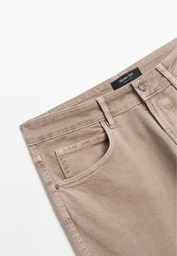 Beżowe dżinsy w wąskim kroju, pięć kieszeni, metalowy guzik oraz stębnowanie, oznaczone metką "Massimo Dutti" w pasie.