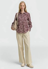 Chemise à manches longues imprimée avec un motif bordeaux et crème, associée à un pantalon large crème et des chaussures à plateforme crème.