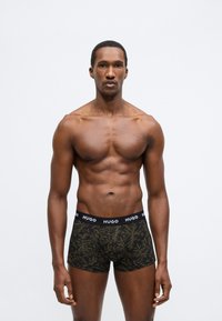 Čierne boxerky s listovým vzorom, s čiernym pásom označeným nápisom "HUGO." Vyrobené z elastického materiálu, navrhnuté pre pohodlie a správne prispôsobenie.