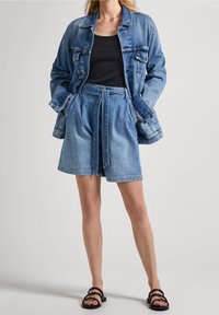 Jeansjacka med en avslappnad passform och klassiska fickor, ihop med högmidjade jeansshorts med ett knytband, båda i ljusblå.