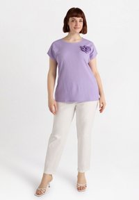 Violetti lyhythihainen paita, jossa on teksturoitu pinta ja kukkaaccentti, yhdistettynä valkoisiin suoriin housuihin ja avokärkisiin korkokenkiin.