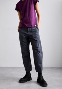 Camiseta corta de manga corta en color púrpura, de corte holgado. Pantalones grises con bolsillos laterales y acabado texturizado. Botines negros con suelas gruesas.