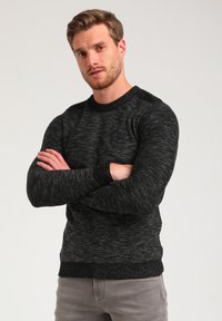 Black and gray speckled knit sweater with a crew neck, ribbed cuffs, and hem. Features a small logo patch on the chest.