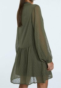 Olivegrünes, leichtes Kleid mit langen, luftig-weiten Ärmeln, strukturierten Punkten und einer gerafften Taille, das oberhalb des Knies endet.