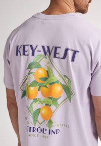 Fialové bavlněné tričko s grafickým designem pomerančů se zelenými listy a textem "KEY-WEST" tučným modrým písmem.
