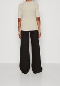 Beige ribbed short-sleeve top with a fitted design, paired with loose black wide-leg pants, showcasing smooth fabric textures.