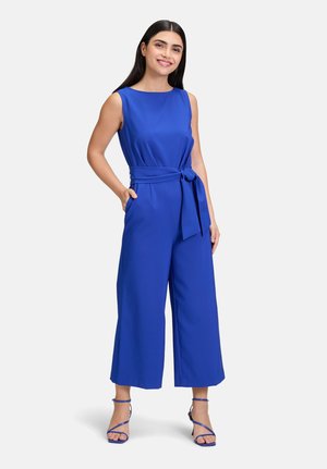 Blå ärmlös jumpsuit med midjeband, vid ben-design, mjuk textur och rundad halsringning. Matchas med blå sandaler med remmar.