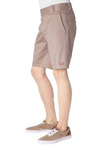Pantaloni corti beige realizzati in materiale misto cotone, con frontale piatto, tasche laterali e una piccola etichetta rossa sul cinturino.
