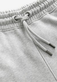 Grå sweatpants har en elastisk talje med snøre, en glat tekstur og metalaccenter på snørebåndsenderne.