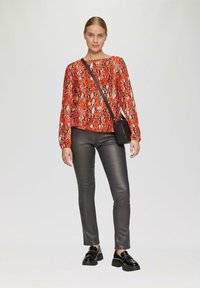 Rood en zwart slangenprint blouse met lange mouwen, gecombineerd met aansluitende zwarte neplederen broek en stevige zwarte loafers, met een kleine zwarte schoudertas.