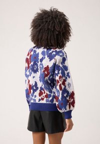 Pletený svetr s květinovým vzorem v modré, červené a bílé barvě; má kulatý výstřih a žebrované manžety a lem; doplněný o černé šortky.