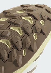 Close-up of a brown and beige rugged shoe sole with angular, textured tread patterns designed for grip and traction.