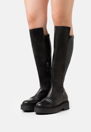 Bottes noires en cuir hauteur genou avec une semelle plate, dotées d'une fermeture éclair latérale et de détails de couture subtils sur la zone des orteils.