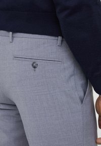 Pantaloni grigi su misura realizzati in stoffa texturizzata; presentano una tasca posteriore con bottone, fronte piatto e un design aderente.