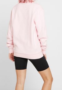 Jasnoróżowa bluza z prążkowanym dołem i mankietami, o luźnym kroju i minimalistycznych detalach szwów, zestawiona z czarnymi krótkimi spodenkami rowerowymi.