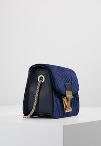 Marineblaues, gesteppte Stoffhandtasche mit strukturierter Form, goldenen Hardware-Akzenten und einer Kettenriemen. Verfügt über einen Klappenverschluss und ein Logo-Detail.