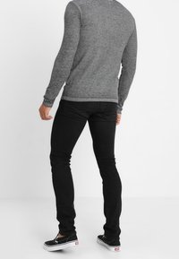 Harmaa pitkähihainen paita yhdistettynä mustiin slim-fit -farkkuihin. Asusteessa on rento muotoilu, pehmeä rakenne ja hienovaraiset ompeluyksityiskohdat.