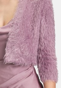 Veste courte en fausse fourrure de couleur violet clair avec une finition texturée et shaggy ; présente des manches trois-quarts et un design à ouverture frontale.