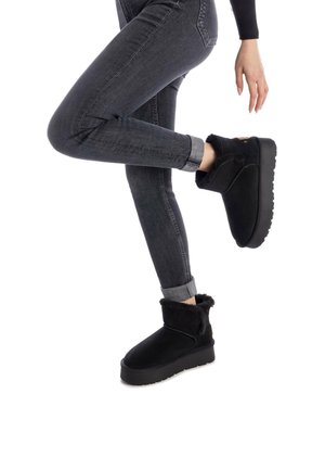 Botines negros con un suave puño forrado de pelo, con una suela resistente, llevados con vaqueros oscuros remangados. Predomina el material de gamuza suave.