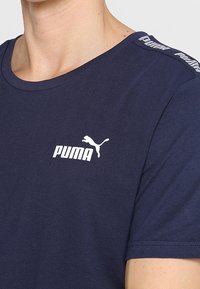 Námořnická modrá bavlněná tričko s kulatým výstřihem, na kterém se nachází bílé logo Puma na hrudi a logo na rameni. Měkká textura.
