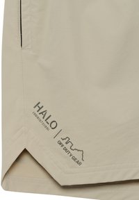 Beige shorts tillverkade av lättviktig tyg, med en subtil lyster, sned nederkant, och tryckt varumärkeslogotyp i mörkgrått. Inkluderar sidofickor med söm.