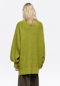 Zielony sweter z dzianiny o luźnym kroju, z prążkowaną strukturą i opuszczonymi ramionami. Posiada szerokie rękawy i nieco dłuższy tylny brzeg.