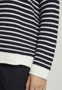 Stickad tröja med marinblå och vita horisontella ränder, texturerad tyg, rund halsringning och ribbad mudd vid ärmar och fåll.