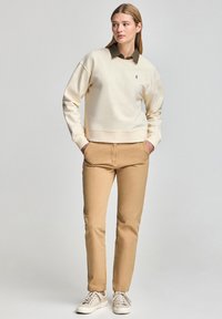 Felpa beige con scollatura rotonda, vestibilità comoda, polsini e orlo a coste. Abbinata a pantaloni beige slim-fit e sneakers beige.