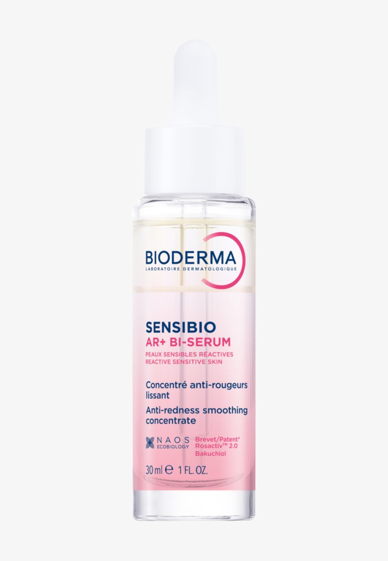 Flacon compte-gouttes en verre transparent avec un liquide rose étiqueté Bioderma Sensibio AR+ Bi-Serum pour peau sensible anti-rougeurs, 30 ml.