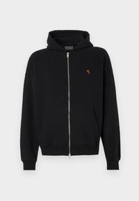 Must värvi tõmblukuga kapuutsiga jakke, mis on valmistatud pehmest kangast, kangaroo taskuga, soonikuga varrukate ja väikese tikandiga logoga rinnal.