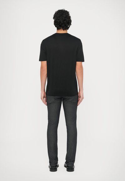 Juoda trumpomis rankovėmis suknelė su klasikinio kirpimo modeliu, derinama su liesais tamsiais džinsais. Apranga pasižymi lygiu paviršiumi ir minimalistiniu dizainu.